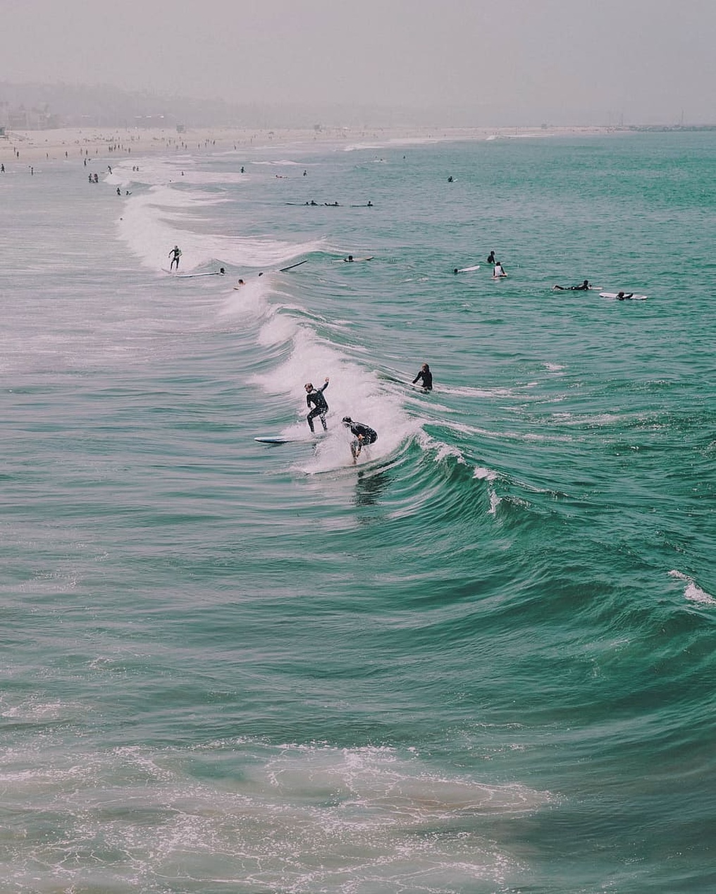 A diverse group of surfers looking at a smartphone together on a beach.