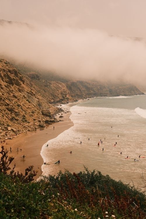 Foggy coastal beach with swimmers, rocky cliffs, and gentle waves