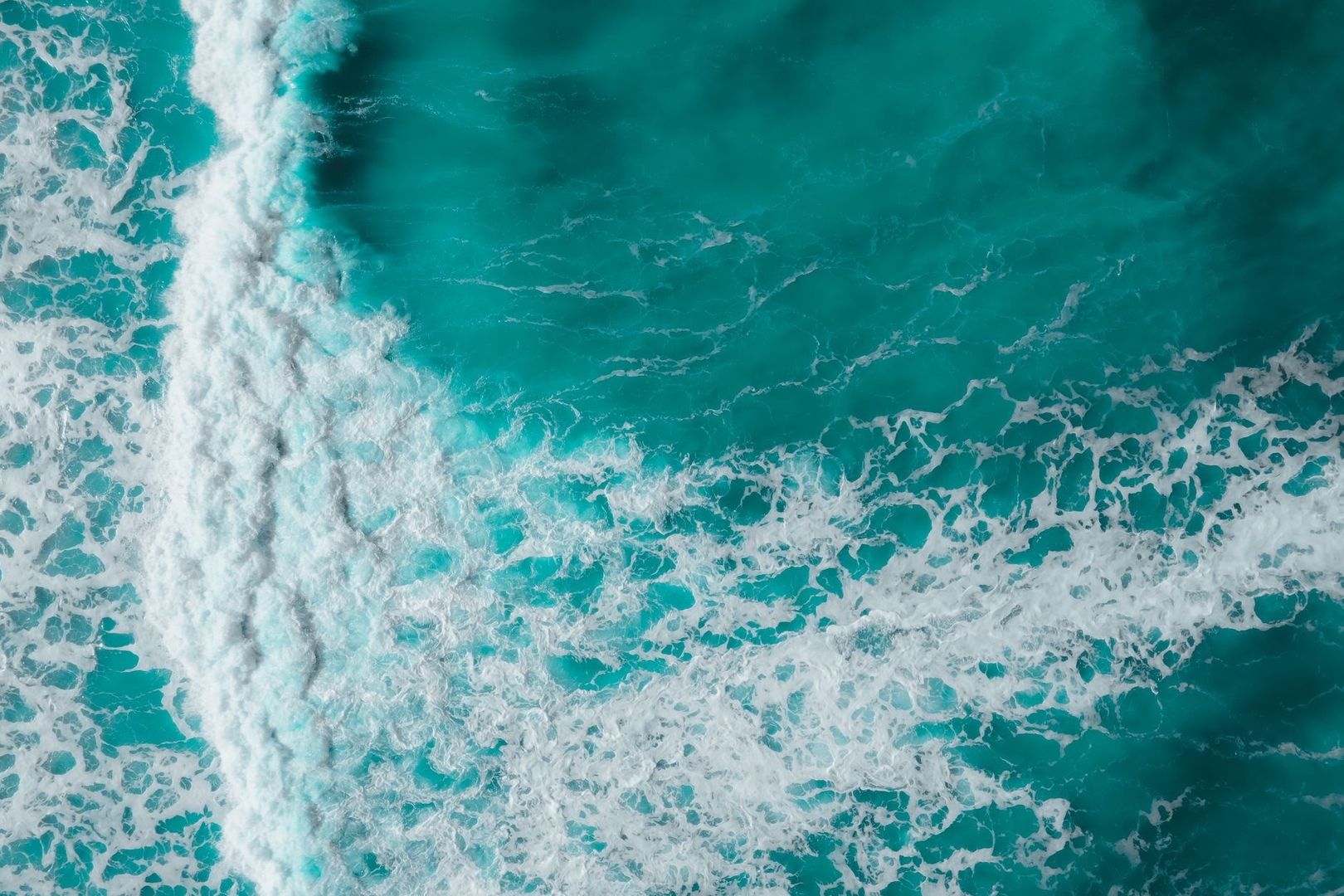 Aerial view of white surf breaking across turquoise ocean water